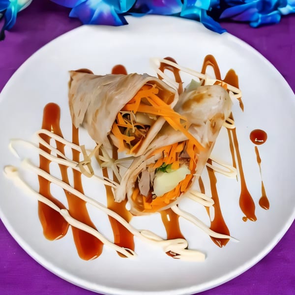 Two savory crepes filled with shredded carrots and meat, drizzled with sauces on a white plate.