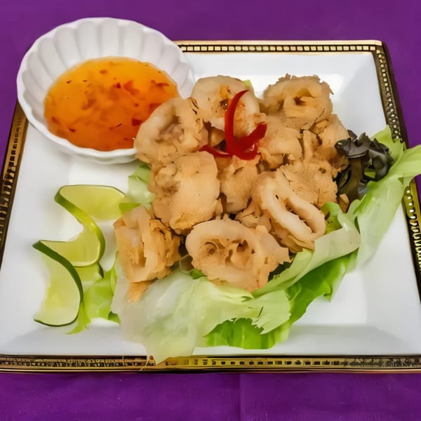 Crispy fried calamari on lettuce with lime wedges and sweet chili sauce on a white plate.