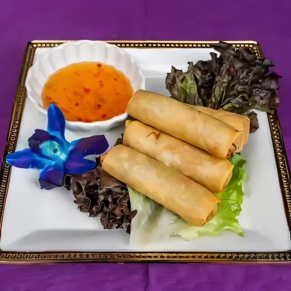 Golden spring rolls with sweet chili sauce, lettuce, and a blue orchid on a white plate.